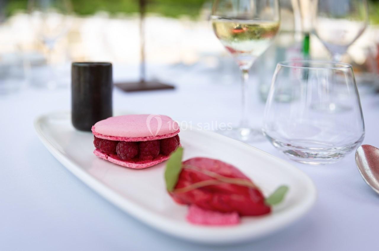Macaron rose garni de framboises fraîches, accompagné d'un sorbet rouge, servi sur une assiette blanche.