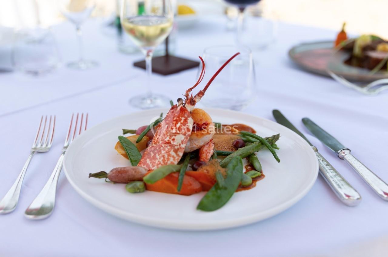 Assiette de homard accompagné de légumes variés, servie sur une table dressée avec couverts et verres à vin.