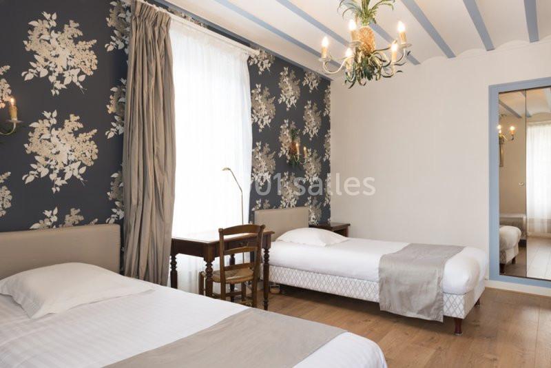 Chambre lumineuse avec deux lits simples, un bureau en bois, un miroir et un papier peint floral sombre.