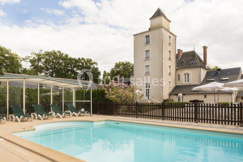 Piscine extérieure avec chaises longues devant un bâtiment historique entouré de verdure.