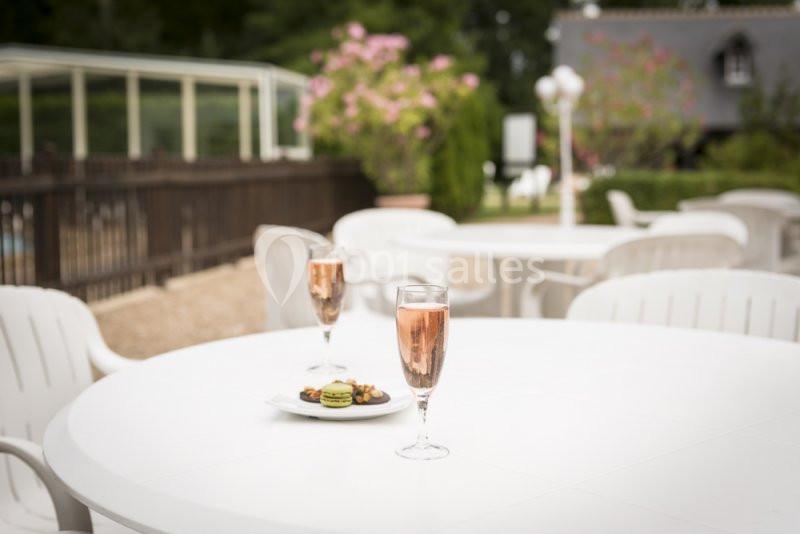 Deux verres de champagne rosé et une assiette de macarons sur une table blanche en terrasse, avec un jardin en arrière-plan.