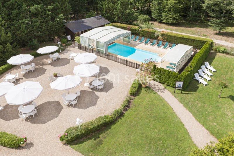 Vue aérienne d'une piscine extérieure couverte entourée de chaises longues, avec des tables et parasols sur une terrasse.