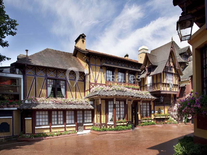 Façade d'un bâtiment à colombages avec des fleurs aux fenêtres, sous un ciel partiellement nuageux.