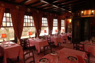 Salle de restaurant élégante avec nappes blanches, grandes fenêtres donnant sur un paysage verdoyant et décoration…