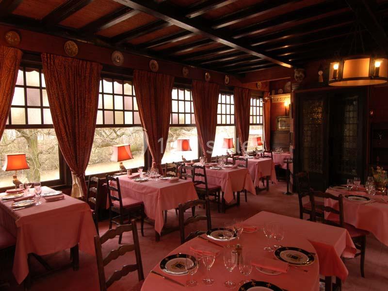 Salle de restaurant chaleureuse avec tables dressées, nappes roses, grandes fenêtres et éclairage tamisé.