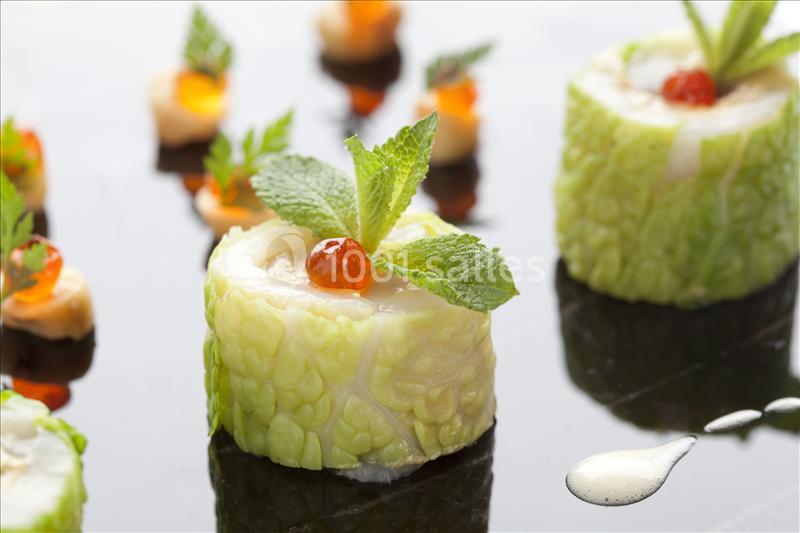 Rouleaux de chou garnis de crème, œufs de poisson et feuilles de menthe, présentés sur une surface brillante.