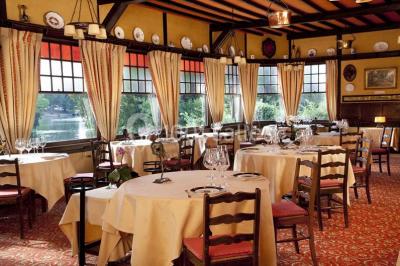Salle de restaurant élégante avec nappes blanches, grandes fenêtres donnant sur un paysage verdoyant et décoration…