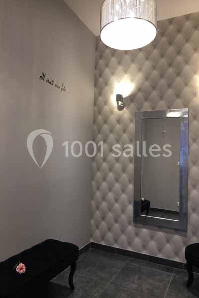 Miroir mural encadré sur un mur texturé, avec un banc noir et un éclairage suspendu dans une pièce sobre.