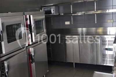Cuisine professionnelle avec équipements en inox, fours encastrés, étagères murales et hotte d'extraction.
