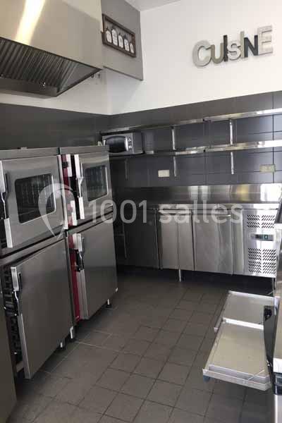 Cuisine professionnelle avec équipements en inox, fours encastrés, étagères murales et hotte d'extraction.