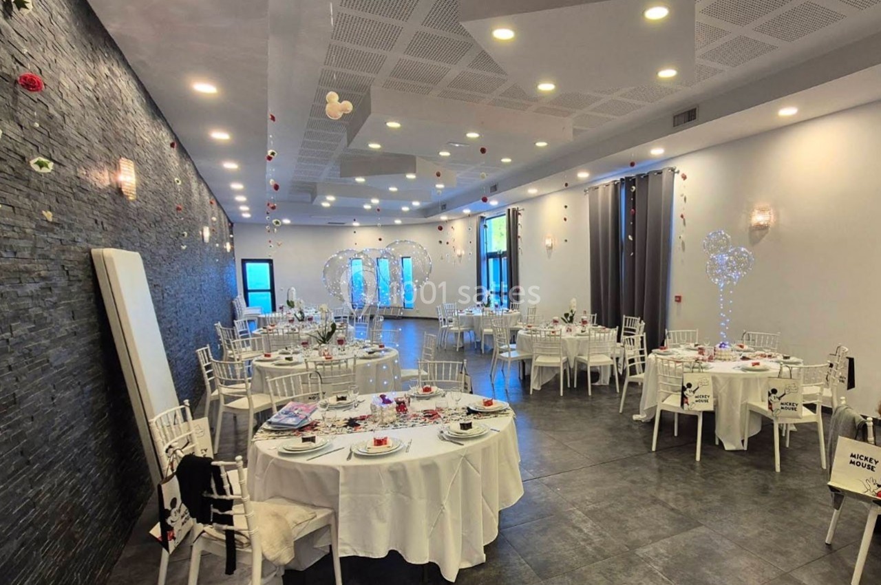Salle de réception décorée avec des tables rondes dressées, des chaises blanches et des ornements lumineux.