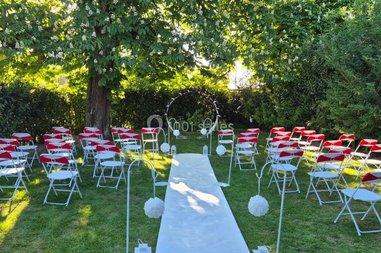 Chaises blanches avec assises rouges disposées en extérieur autour d'une allée centrale menant à une arche décorée.