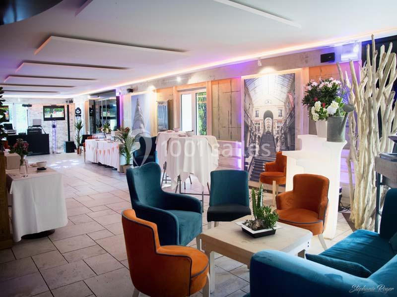 Salle lumineuse aménagée avec des fauteuils colorés, des tables hautes et une décoration moderne et végétale.