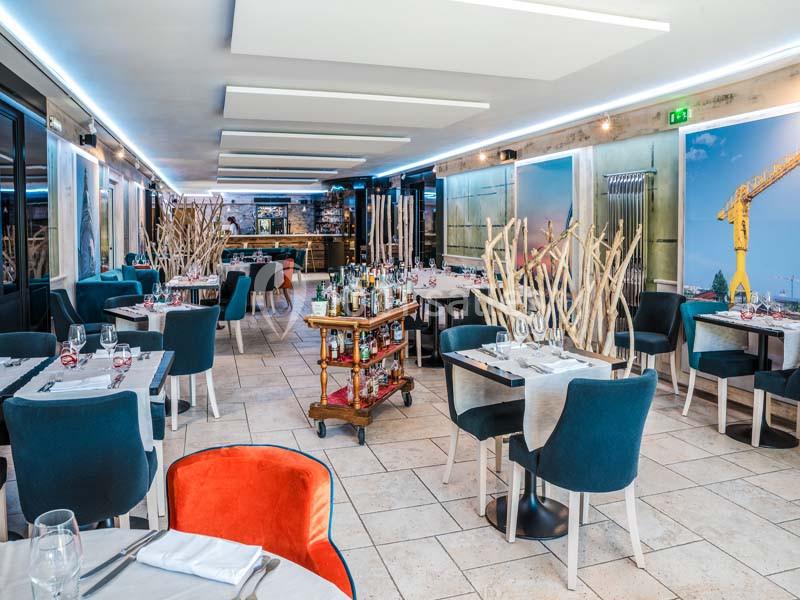 Salle de restaurant moderne avec tables dressées, chaises bleues, décoration épurée et un chariot de service au centre.