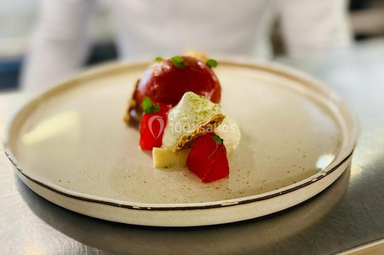 Dessert raffiné composé de fruits rouges, crème, biscuit croustillant et touches de verdure, présenté sur une assiette beige.