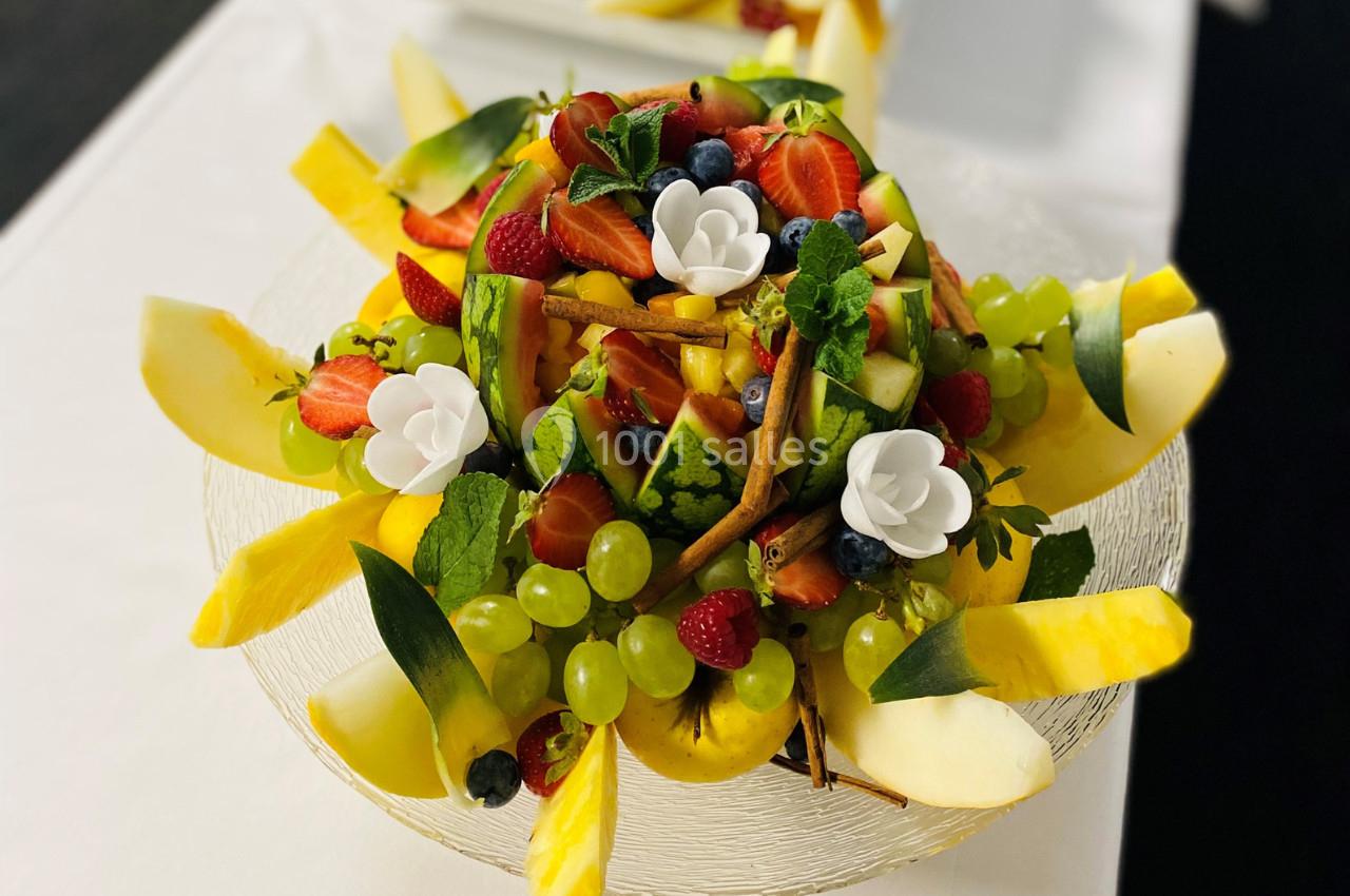 Assiette garnie de fruits variés tels que fraises, raisins, ananas et framboises, décorée de fleurs en sucre.
