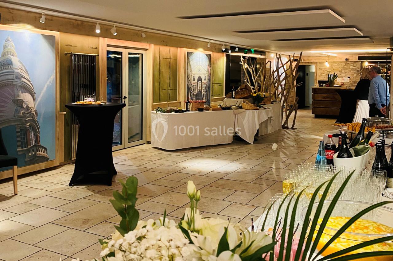 Salle lumineuse aménagée pour un buffet, avec tables garnies de boissons, plats et décorations florales.