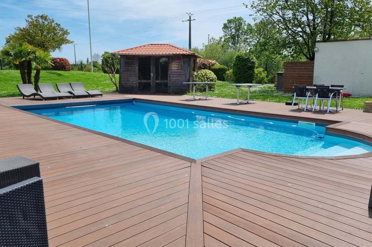 Piscine extérieure entourée d'une terrasse en bois avec chaises longues, mobilier de jardin et cabanon en arrière-plan.