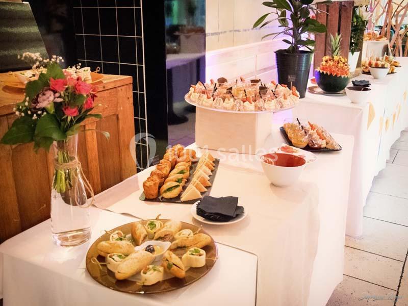 Buffet avec divers amuse-bouches, sandwichs, viennoiseries et fleurs en décoration sur des tables blanches.