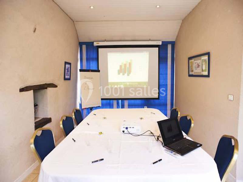 Salle de réunion avec une table blanche, un projecteur affichant un graphique, un tableau blanc et des chaises bleues.