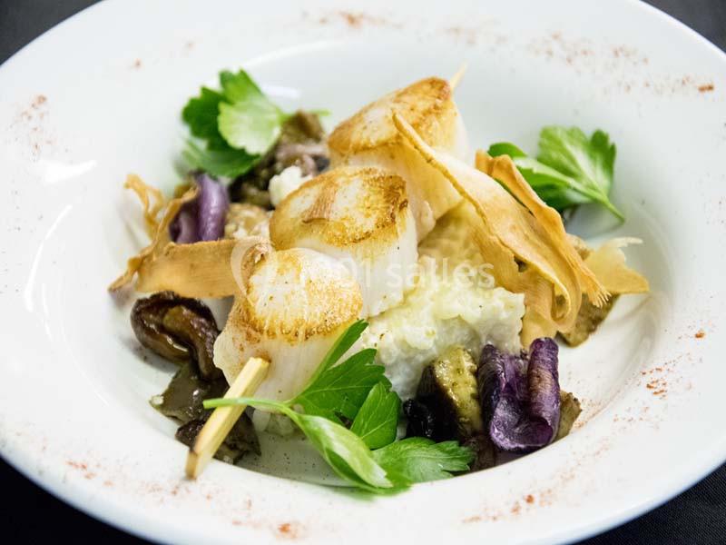 Brochette de noix de Saint-Jacques grillées servie sur un lit de purée et légumes, décorée de feuilles de persil.