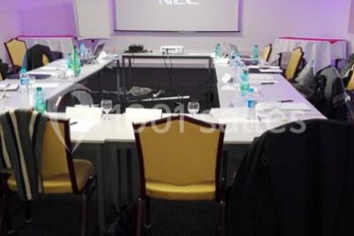 Piscine extérieure entourée de chaises longues et parasols, avec des bâtiments en arrière-plan sous un ciel dégagé.