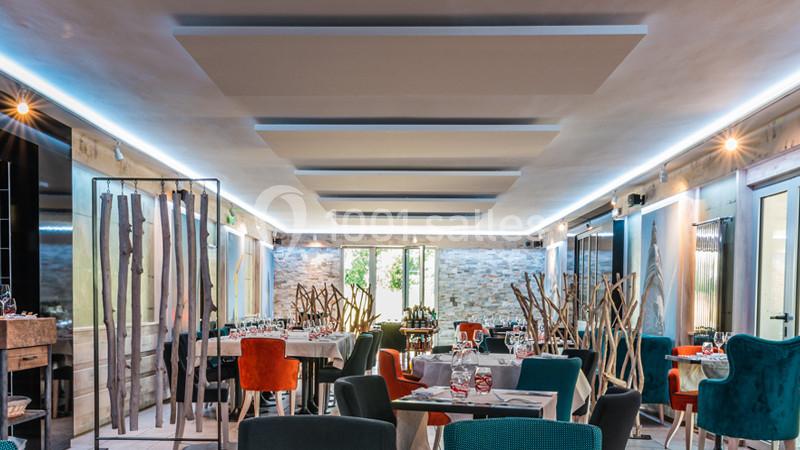 Salle de restaurant moderne avec tables dressées, chaises colorées et lumière naturelle entrant par une baie vitrée.