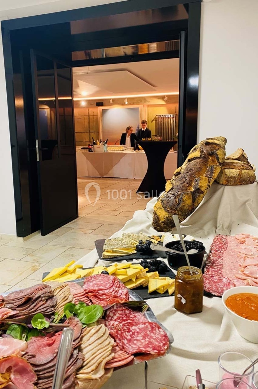 Plateau de charcuteries, fromages, pain et condiments sur une table, avec un buffet en arrière-plan.
