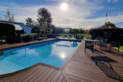 Piscine extérieure entourée de chaises longues et parasols, avec des bâtiments en arrière-plan sous un ciel dégagé.