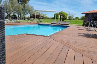 Piscine extérieure entourée de chaises longues et parasols, avec des bâtiments en arrière-plan sous un ciel dégagé.