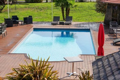 Piscine extérieure entourée de chaises longues et parasols, avec des bâtiments en arrière-plan sous un ciel dégagé.