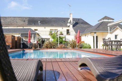 Piscine extérieure entourée de chaises longues et parasols, avec des bâtiments en arrière-plan sous un ciel dégagé.