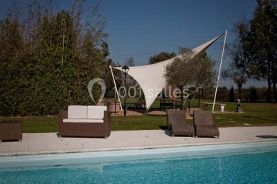 Piscine extérieure entourée de chaises longues et parasols, avec des bâtiments en arrière-plan sous un ciel dégagé.
