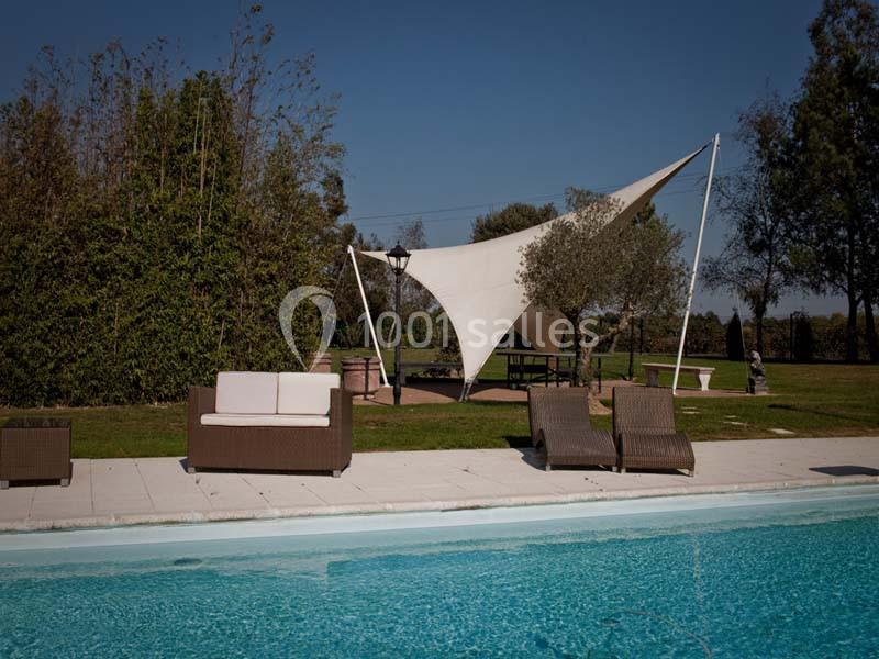 Piscine extérieure avec mobilier en rotin, voile d'ombrage blanche et arbres en arrière-plan.