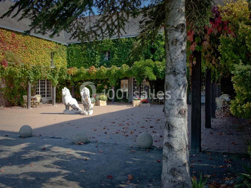 Cour pavée entourée de bâtiments recouverts de lierre, avec deux statues de lions blancs et des tables en arrière-plan.