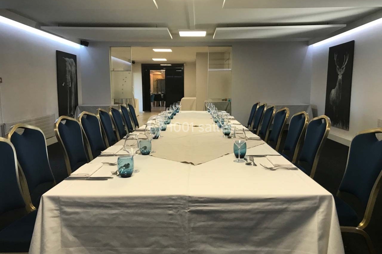 Salle de réunion avec une grande table en U, nappée de blanc, entourée de chaises bleues et décorée de verres turquoise.