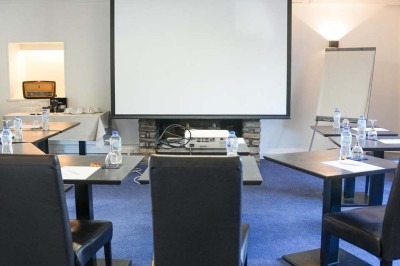 Piscine extérieure entourée de chaises longues et parasols, avec des bâtiments en arrière-plan sous un ciel dégagé.
