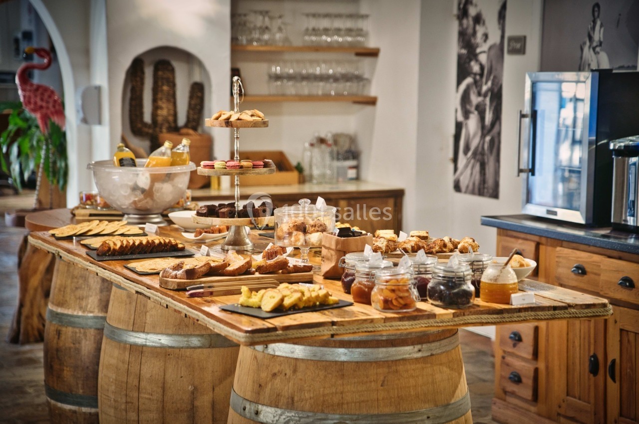Buffet varié disposé sur des tonneaux en bois, avec pâtisseries, fruits et boissons dans un cadre rustique.