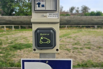 Borne de recharge électrique Green'up installée sur un parking extérieur, avec panneau signalant une place dédiée.