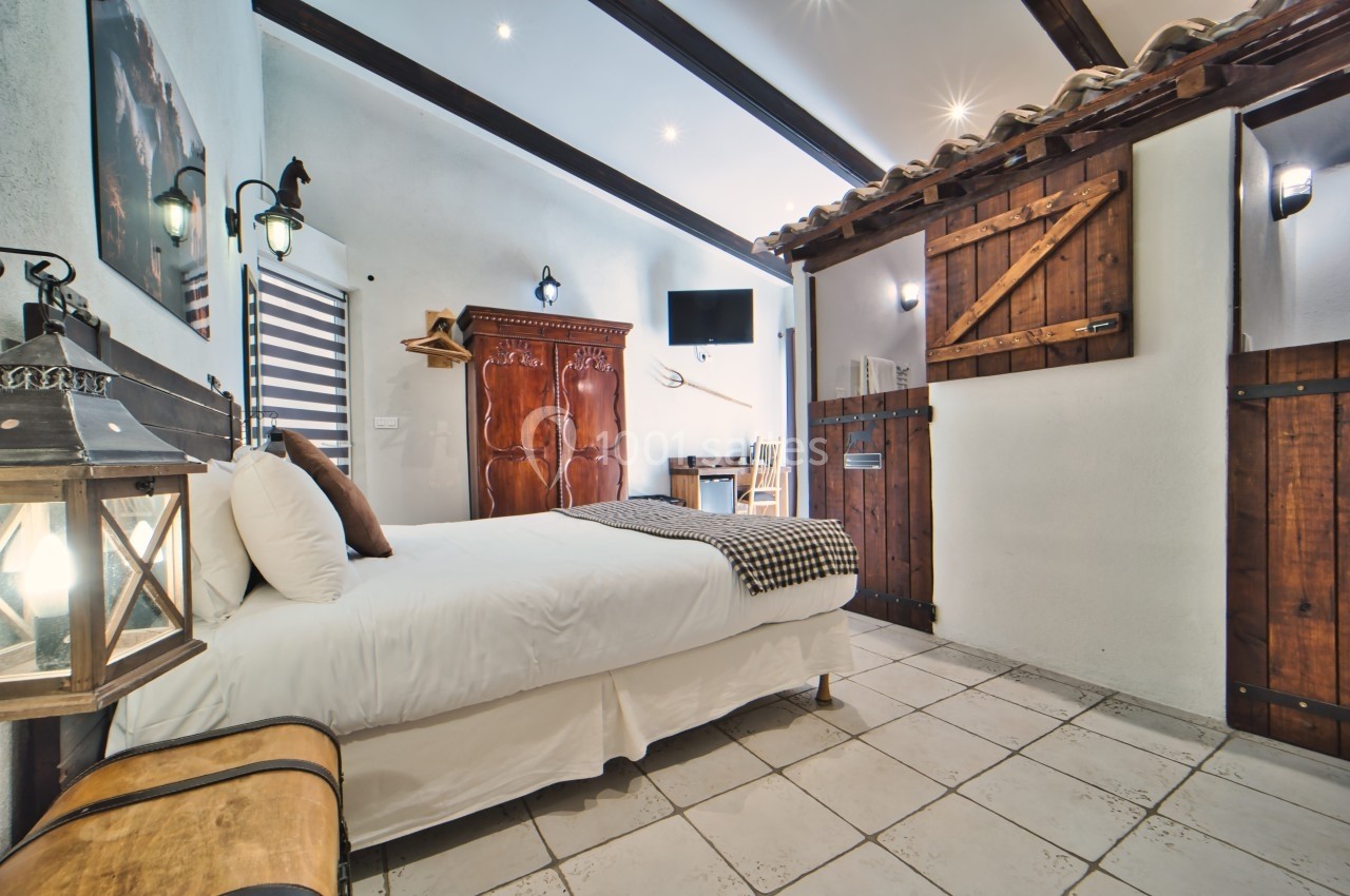 Chambre lumineuse avec lit double, armoire en bois, bureau, télévision murale et décoration rustique.
