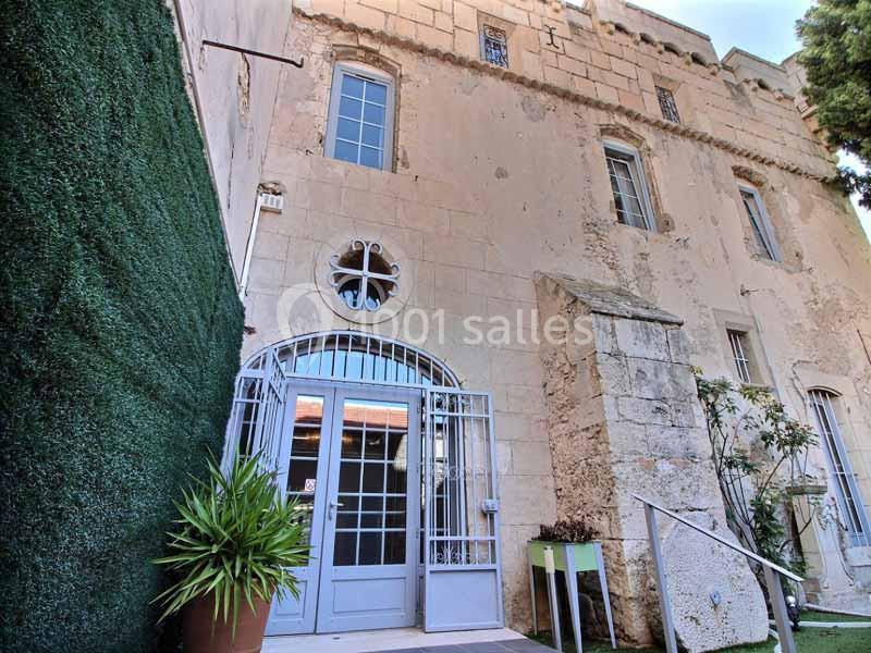Façade en pierre d'un bâtiment ancien avec porte vitrée, fenêtres, plantes en pot et mur végétal à gauche.