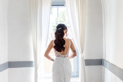 Femme en robe de mariée blanche avec dos en dentelle transparente, montant un escalier intérieur en pierre.