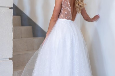 Femme en robe de mariée blanche avec dos en dentelle transparente, montant un escalier intérieur en pierre.