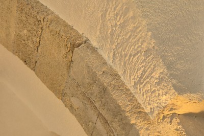 Femme en robe de mariée blanche avec dos en dentelle transparente, montant un escalier intérieur en pierre.