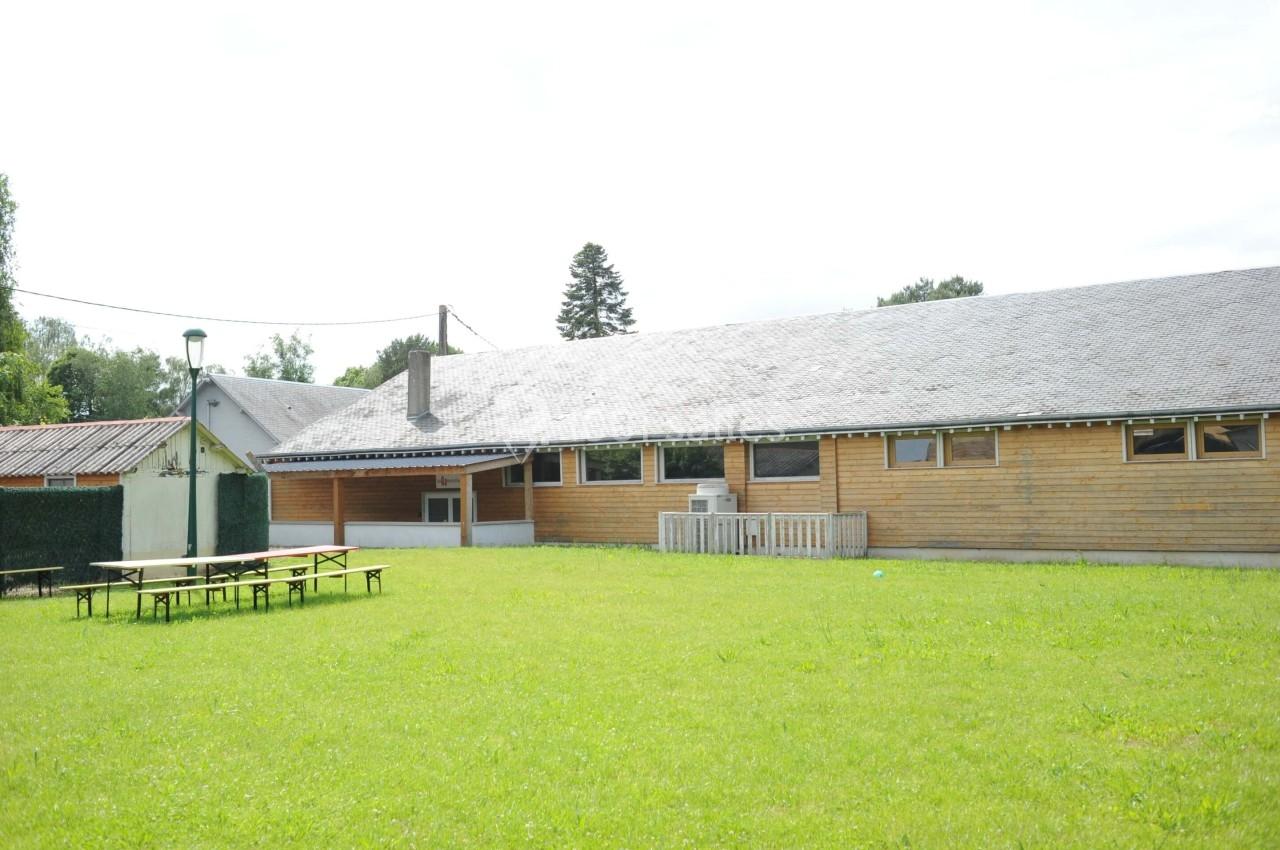 Bâtiment en bois avec toit en ardoise, entouré d'une pelouse, tables de pique-nique au premier plan.