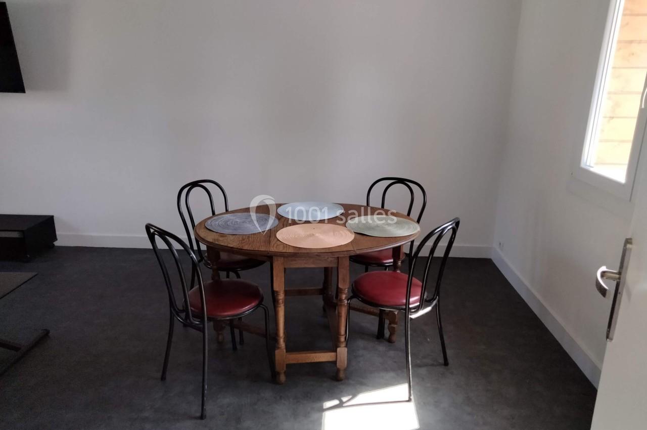 Table ronde en bois avec quatre chaises noires et des sets de table colorés dans une pièce lumineuse au sol sombre.