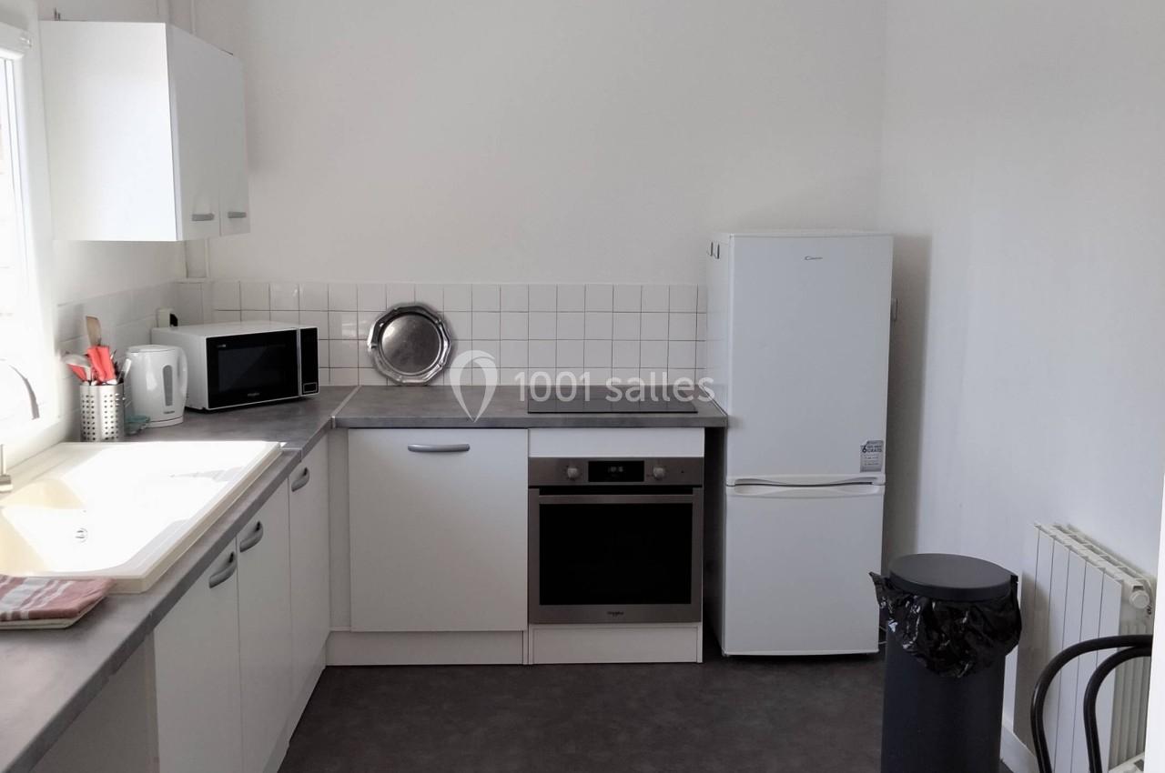 Cuisine moderne avec meubles blancs, réfrigérateur, four encastré, évier, micro-ondes et poubelle sur un sol gris.