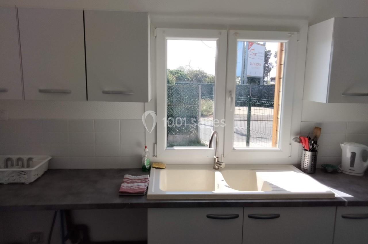 Évier de cuisine sous une fenêtre, entouré de placards blancs, avec quelques ustensiles et un égouttoir sur le plan de…