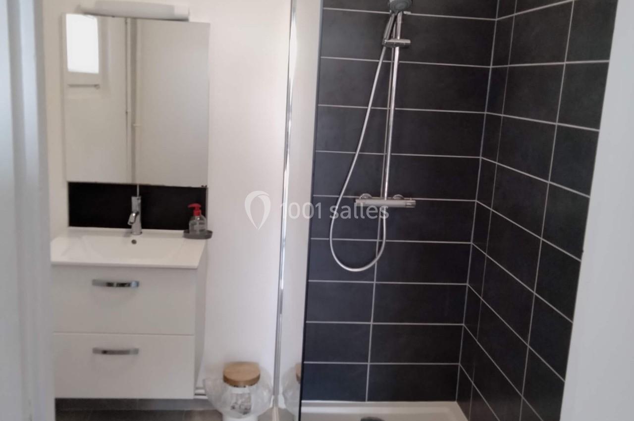 Salle de bain moderne avec douche à l'italienne, carrelage noir, meuble lavabo blanc et miroir éclairé.