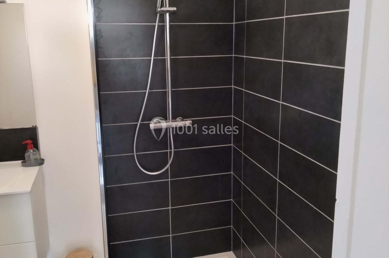 Douche moderne avec paroi vitrée, carrelage noir, pommeau de douche et mitigeur, située dans une salle de bain lumineuse.